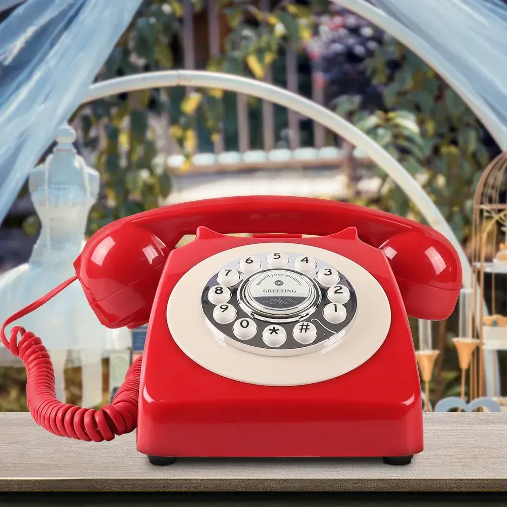 Telefon roșu cu tastatură albă, pe o masă de lemn, în fața unui arc de grădină