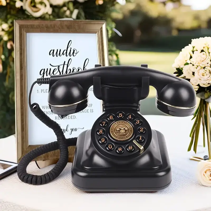 Telefon retro negru Elegance70 Black pe o masă cu flori și un panou audio guestbook